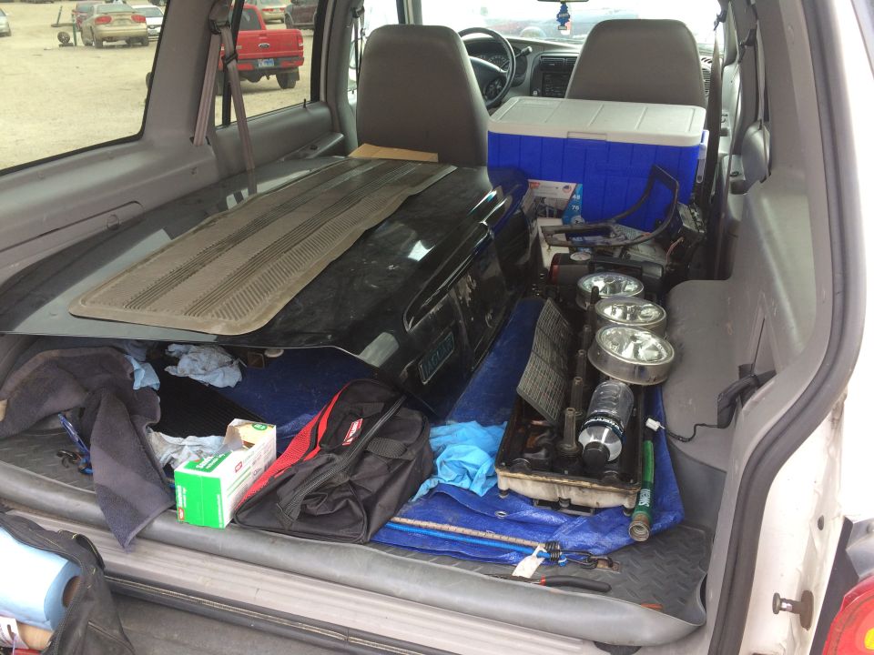Interior of a white SUV loaded with car parts and a cooler.