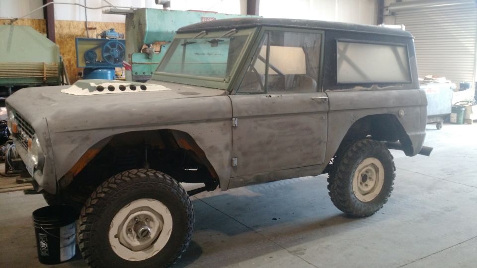 1971 Ford Bronco in primer with modified hood, parked in a workshop.