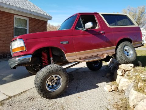 1995 Ford Bronco - A red 1995 Ford Bronco is shown with its front driver's side tire elevated on a pile of rocks, demonstrating its off-road capabilities. The…