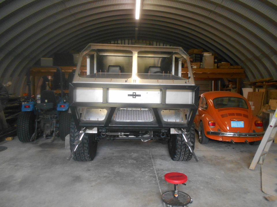 Custom vehicle build in garage with orange VW Beetle and blue tractor.
