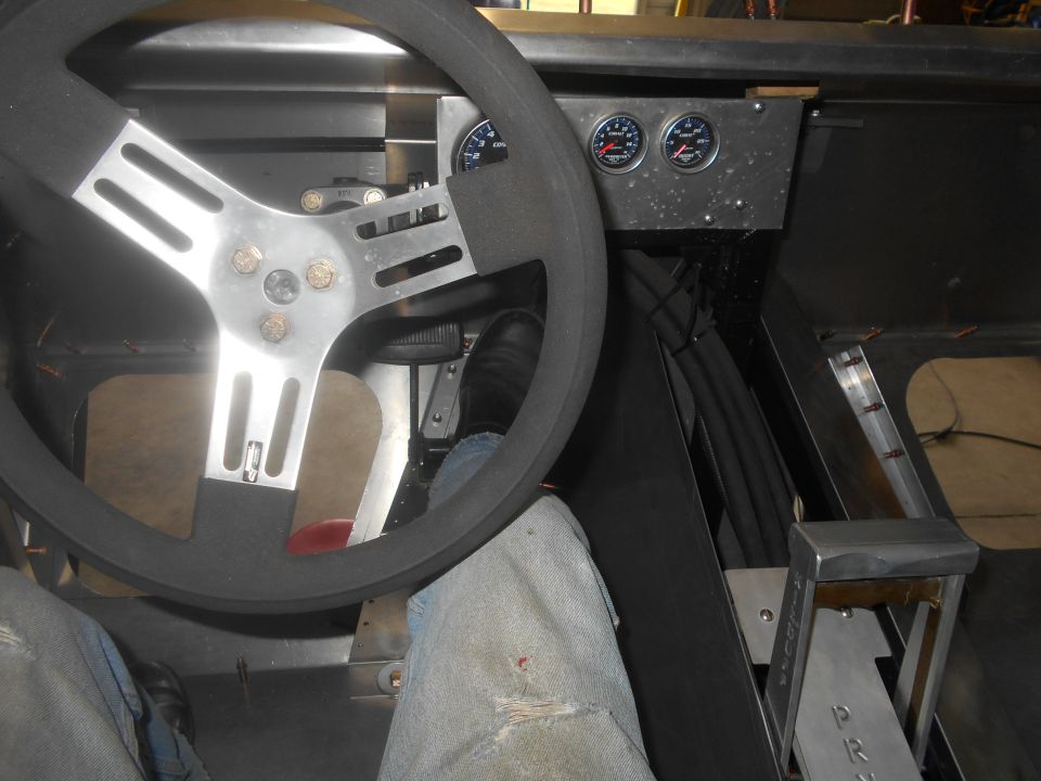 Interior of custom vehicle: steering wheel, gauges, gear shifter, driver's legs.