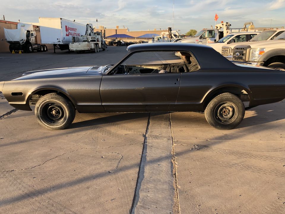 Side view of a dark gray 1968 Mercury Cougar coupe, possibly undergoing restoration.