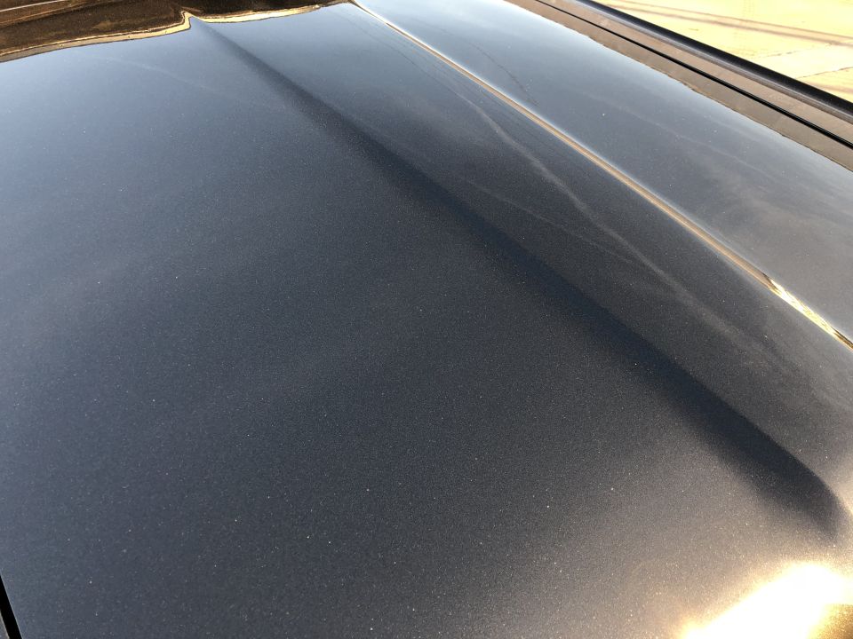 Close-up of a car hood with metallic dark gray paint and a central body line.