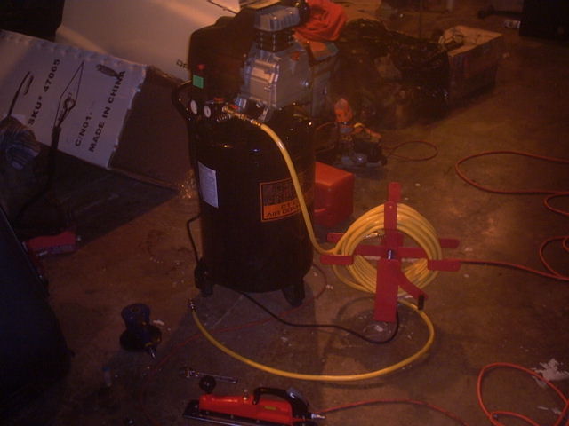 Black air compressor with yellow hose and red tool
