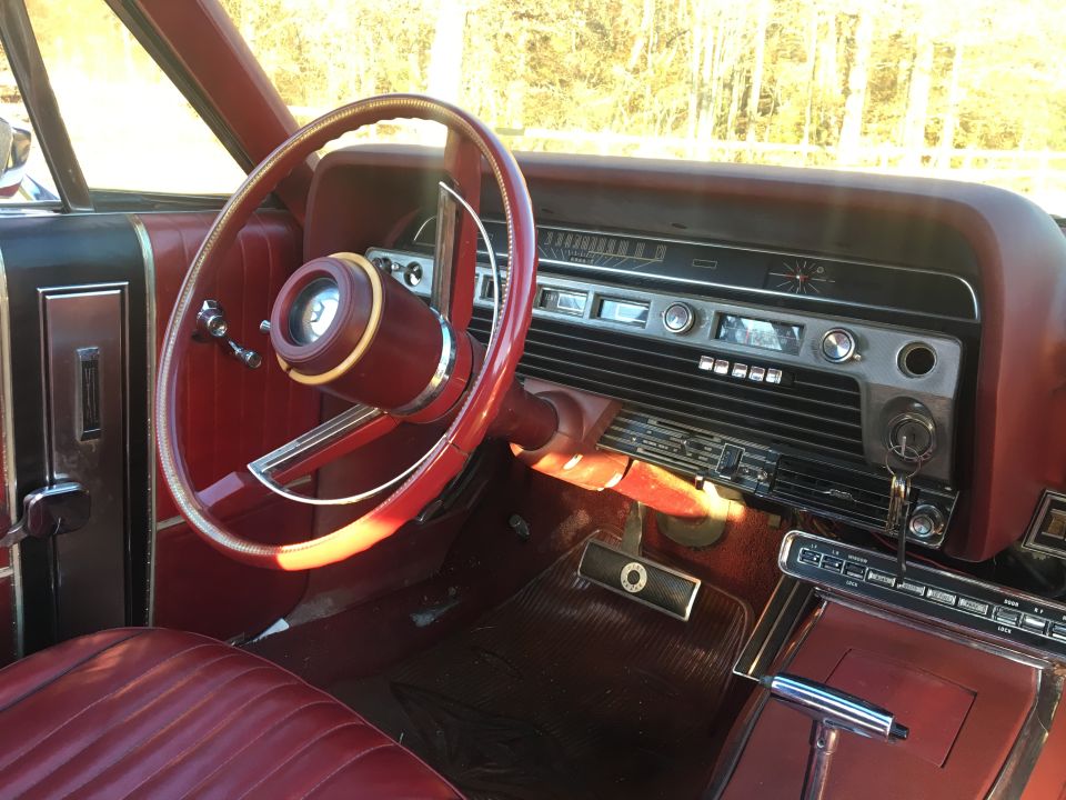 Interior of a classic red Ford Galaxie showing steering wheel, dashboard, radio, and seats.
