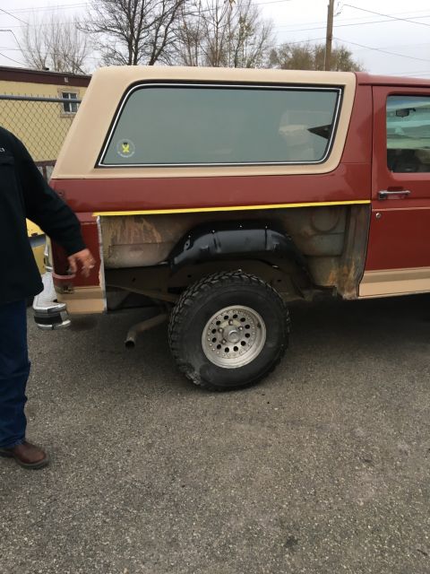 1985 Ford Bronco - The rear passenger side of a vintage maroon and tan SUV is shown with the rear fender removed, revealing the wheel well and suspension comp…