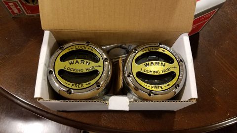 1994 Ford Bronco - A pair of new WARN locking hubs are shown inside their cardboard packaging, sitting on a wooden table.