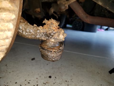 1971 Ford Mustang - A close-up view of a heavily corroded and mud-covered tie rod end assembly on a vehicle. The surrounding area shows dirt and debris on a co…