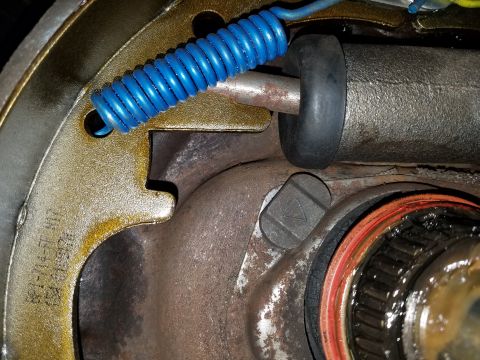 1971 Ford Mustang - A close-up view of the internal components of a drum brake assembly, showing a blue return spring, a wheel cylinder, and part of a hub with…