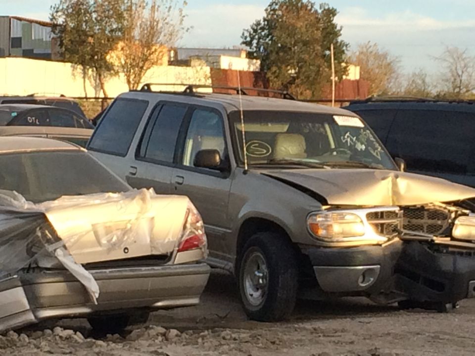 Damaged gold SUV with dented hood and front bumper, parked next to another car covered in plastic