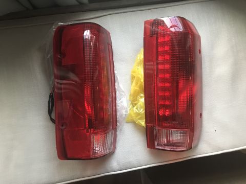 1989 Ford Bronco - Pair of red tail lights shown, one still in protective plastic packaging.