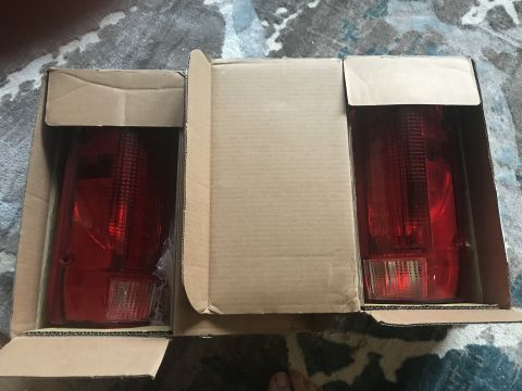 1989 Ford Bronco - A pair of new tail lights are packaged in cardboard boxes, ready for installation.