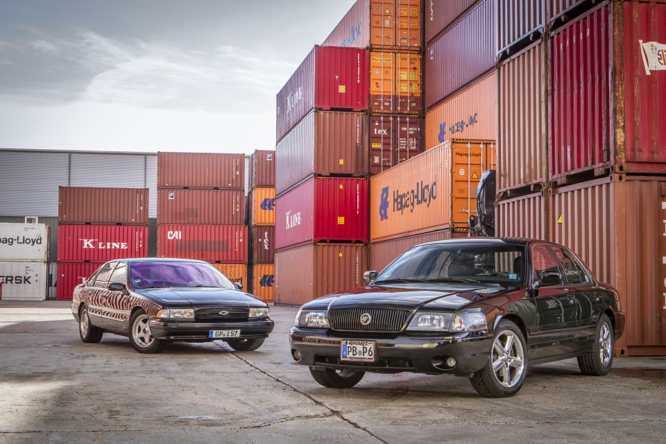 Black 2003 Mercury Marauder parked next to an older black sedan, shipping containers in background