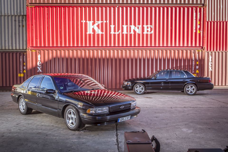 Black Chevrolet Caprice and Mercury Grand Marquis parked in front of shipping containers