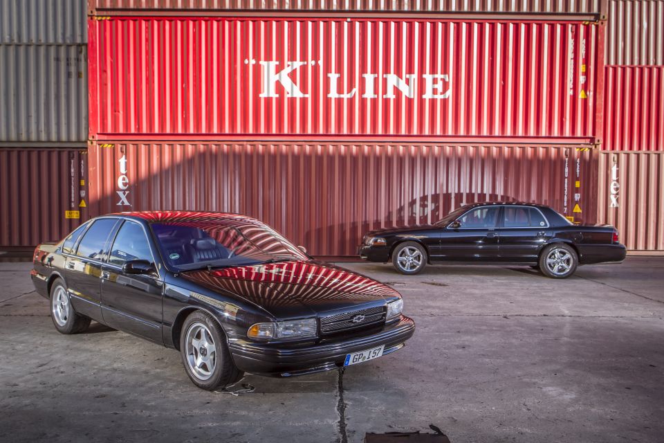 Black sedan with Chevrolet badge in front of red shipping containers