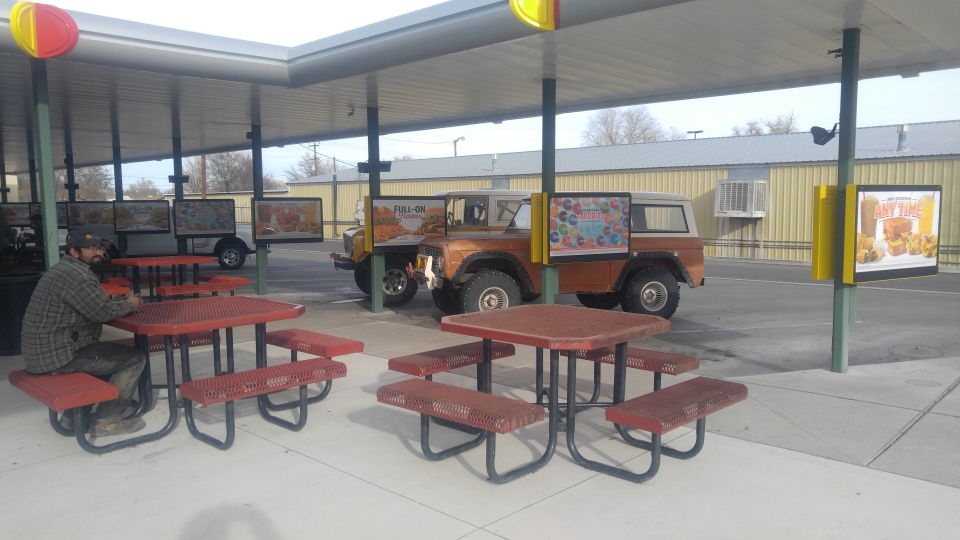 Orange SUV parked under a covered drive-thru area, with a man sitting at a picnic table