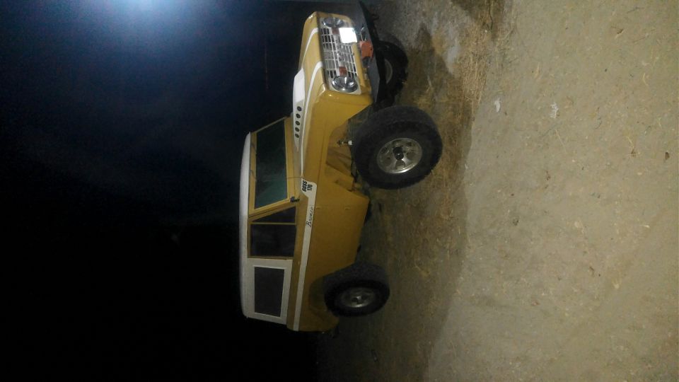 Yellow 1970s Ford Bronco with white top and side trim, parked on dirt