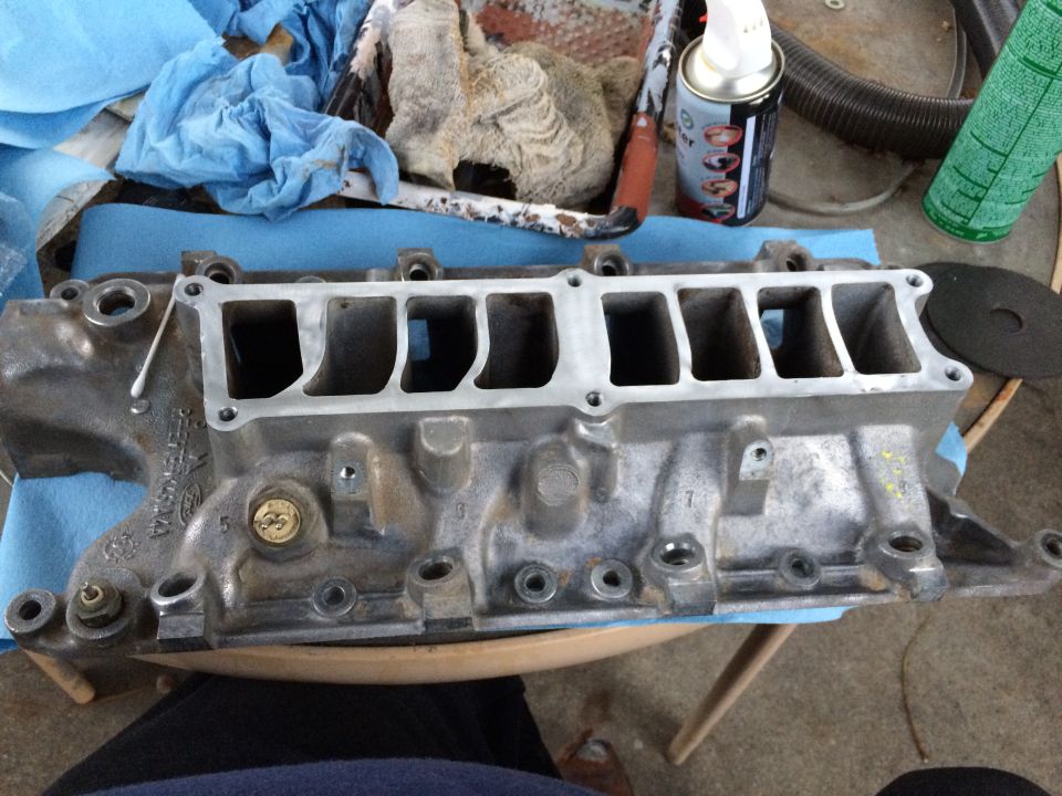 Close-up of an aluminum intake manifold with eight ports. Some cleaning supplies and rags are in the background
