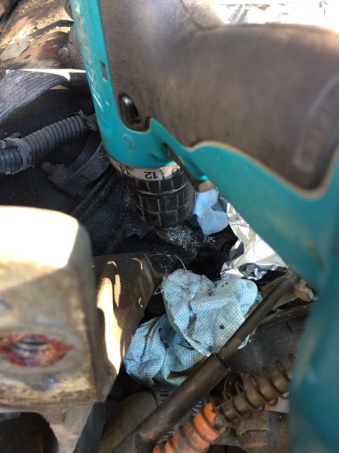 1989 Ford Bronco - Close-up of a drill being used on an engine block, with blue shop towels scattered around.