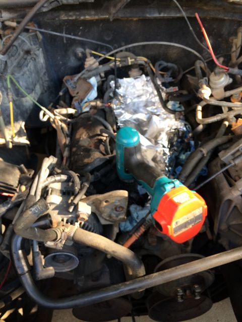 1989 Ford Bronco - The engine bay is cluttered with hoses, wires, and a drill. Foil covers some components.