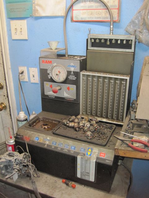 1989 Ford Bronco - A fuel injector cleaning machine is shown with various parts and tools in a workshop setting.