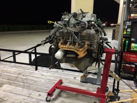 1989 Ford Bronco - Engine on a trailer at a gas station, with a red engine stand supporting it.