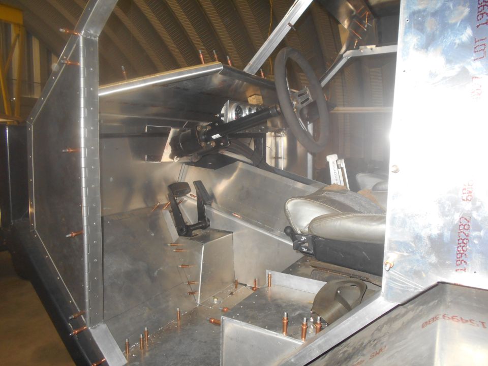 unfinished vehicle interior with steering wheel, pedals, and seats visible
