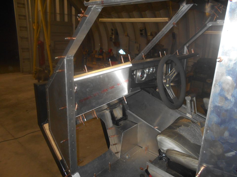 Interior of a custom-built vehicle under construction, showing unfinished metal panels, dashboard, steering wheel, and seat