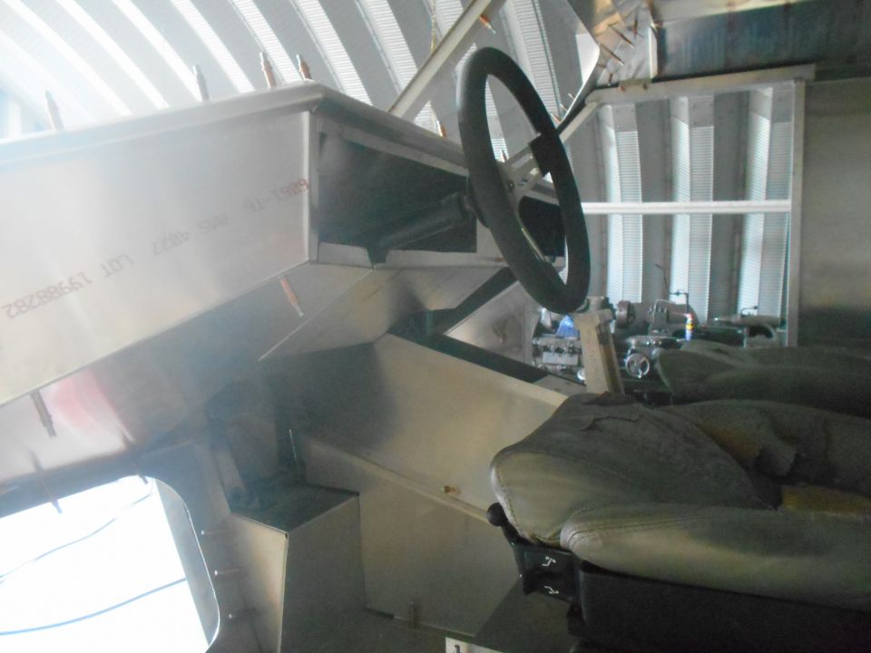 Vehicle interior with metal dashboard, steering wheel, and seat. Text visible on dashboard