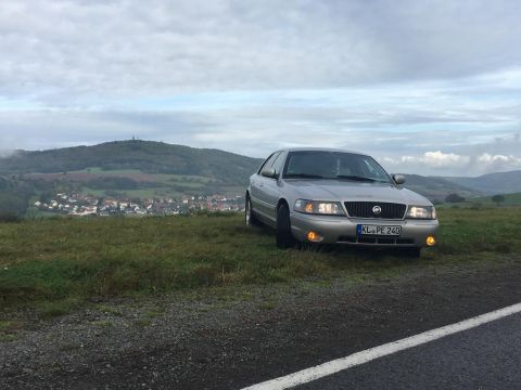 2003 Mercury Marauder - A silver sedan is parked on a grassy hill overlooking a town and rolling hills under a cloudy sky.