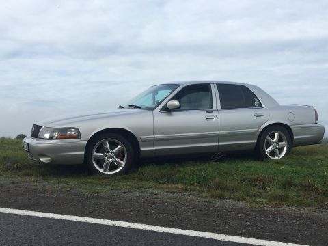 2003 Mercury Marauder - A silver 2003 Mercury Marauder sedan is parked on the side of a road under an overcast sky.