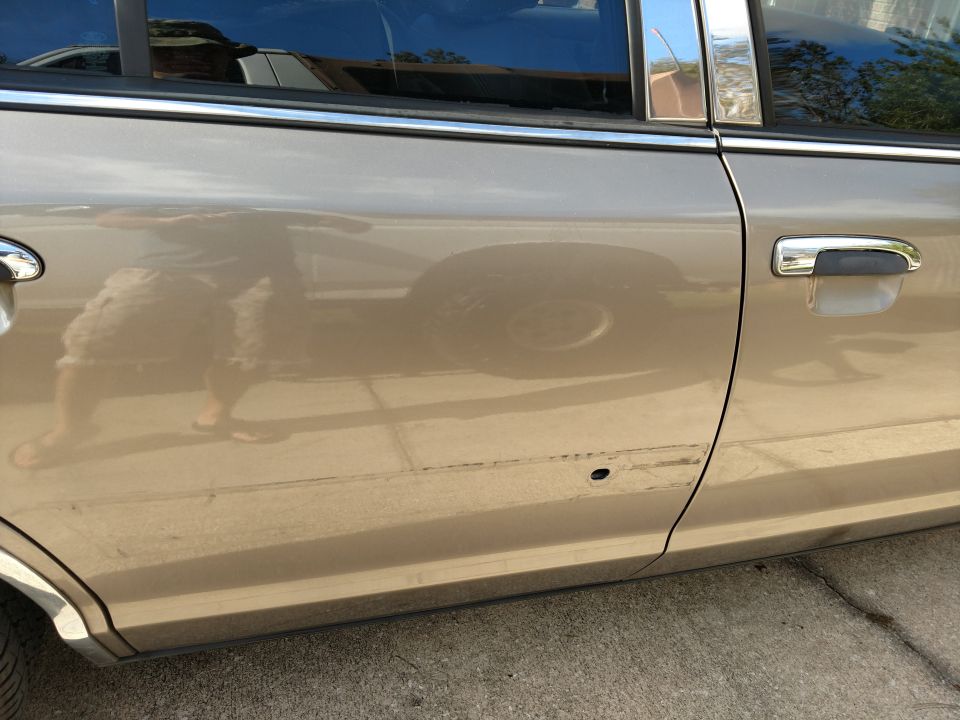 Tan sedan side door with chrome trim and handle, showing damage