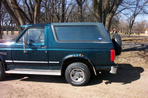 1995 Ford Bronco - Side profile of a 1995 Ford Bronco, showing its dark green paint and removable hardtop.