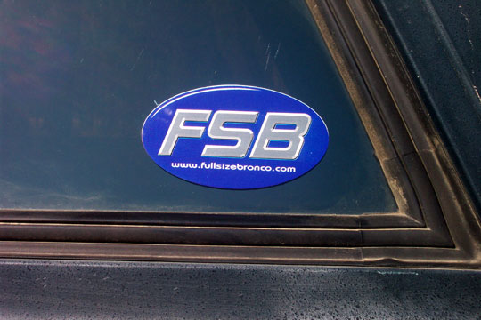 Blue oval sticker with FSB and www.fullsizebronco.com on a dark vehicle