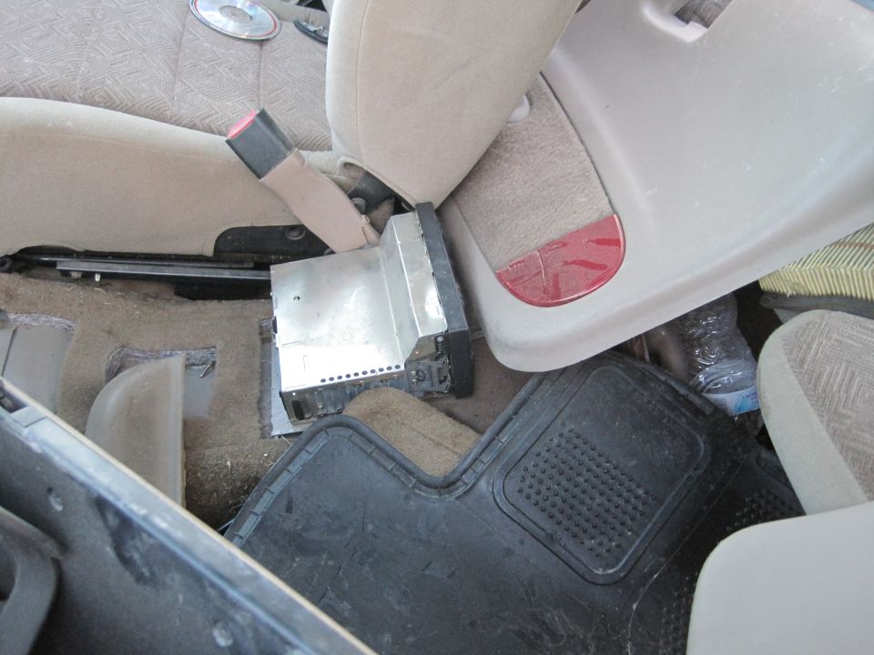 Car interior showing a loose aftermarket stereo unit on the floor, with seats and floor mats visible