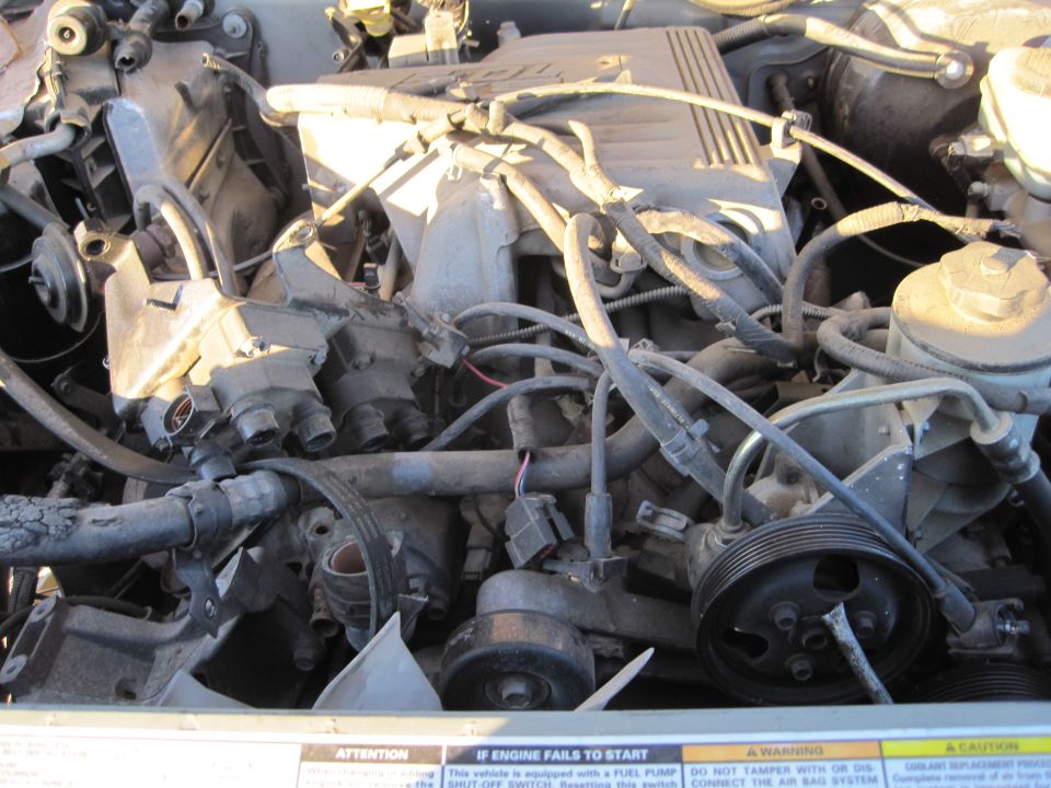 Engine bay with hoses, belts, and engine components visible. Some text labels are present at the bottom