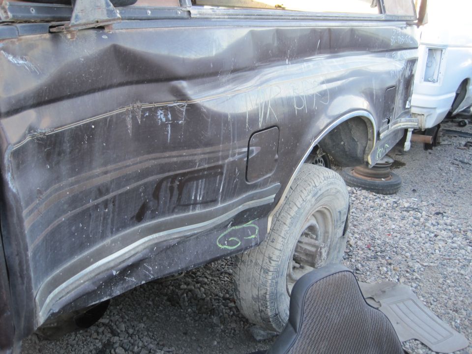 Dark brown truck rear quarter panel with significant damage, dented body lines, and a fuel door