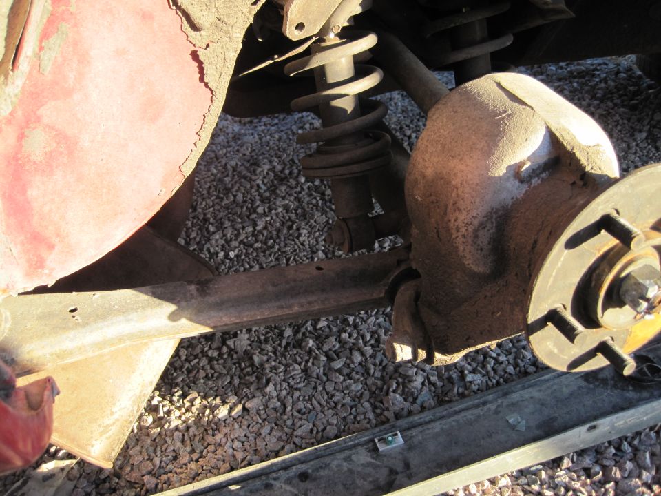 Red car fender fragment above rusty suspension components and brake rotor