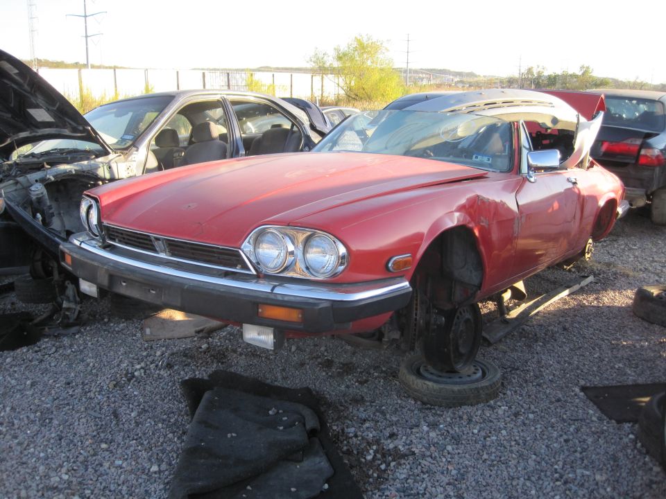 Red coupe with missing wheels, hood open, and dented fender
