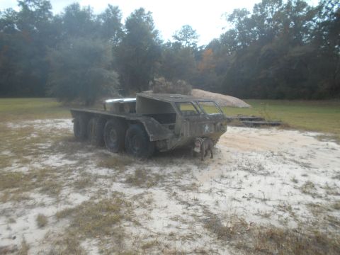 1992 Ford Bronco - A six-wheeled military truck sits in a sandy, grassy area with a dog standing near its front.