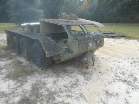 1992 Ford Bronco - A weathered, six-wheeled military truck sits on sandy ground with a bulldog nearby.