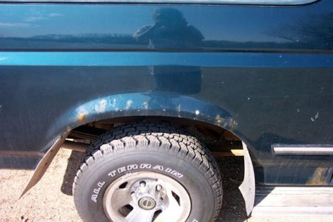 1995 Ford Bronco - The rear quarter panel and wheel well of a dark teal Ford Bronco show significant rust damage.