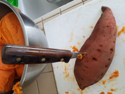 1990 Ford Bronco - A knife is used to peel a sweet potato, with the peeled flesh accumulating in a metal bowl.