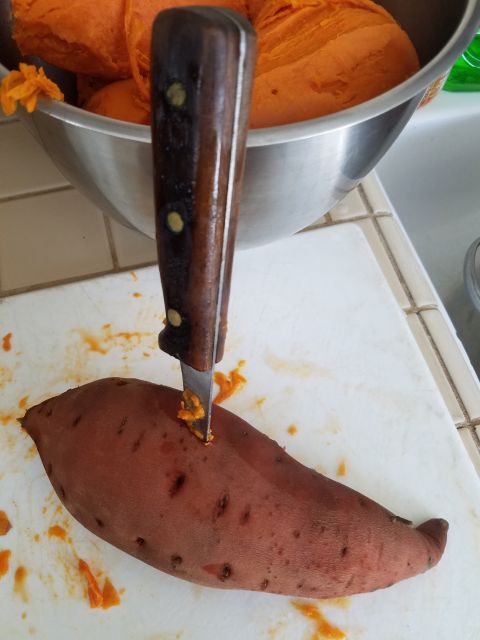 1990 Ford Bronco - A knife is plunged into a sweet potato, with a bowl of peeled sweet potatoes behind it.