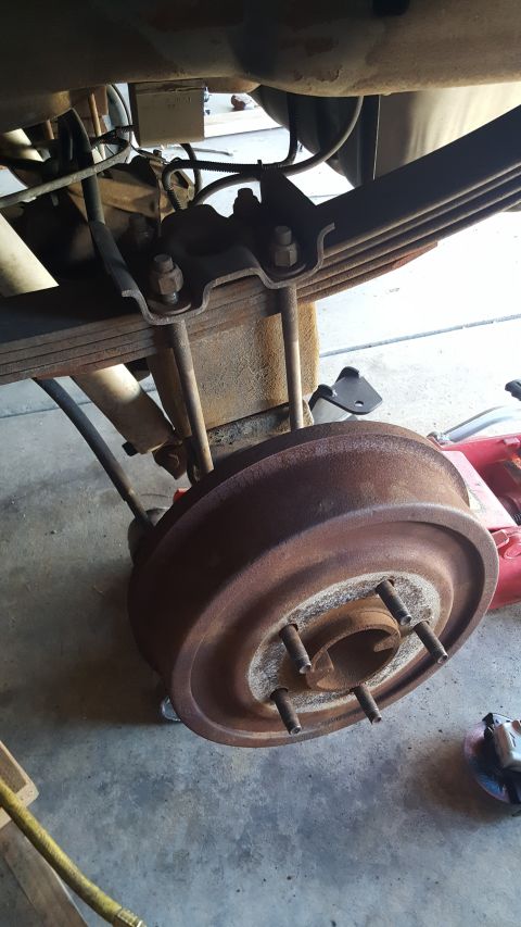 1996 Ford Bronco - Close-up of a rusty drum brake assembly on a vehicle's rear axle, showing leaf springs and a shock absorber.