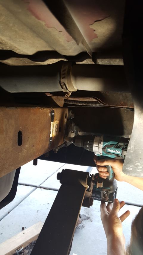 1996 Ford Bronco - Mechanic uses a drill to modify the frame of a vehicle, possibly for a shackle flip modification.