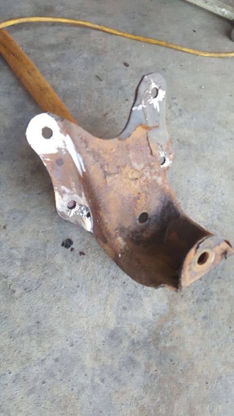 1996 Ford Bronco - A rusty metal suspension part, possibly for a vehicle, lies on a concrete surface with a wooden handle nearby.