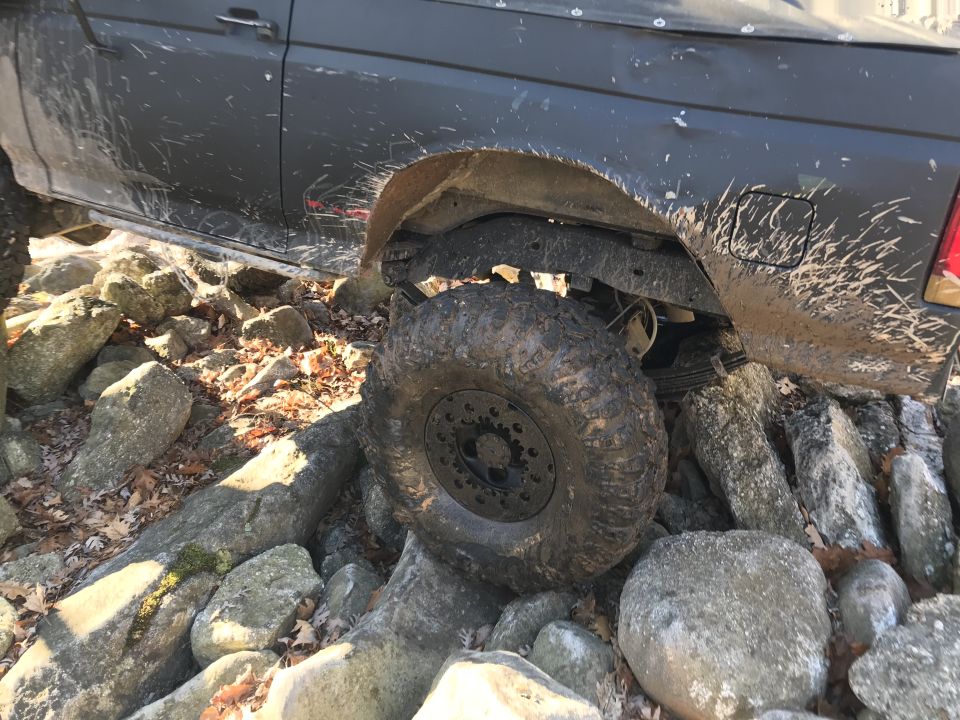 1989 Ford Bronco navigating rocky terrain, mud splattered on body