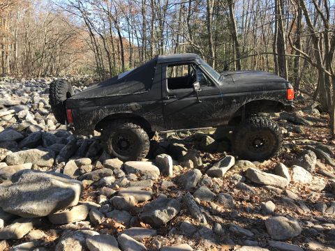 1989 Ford Bronco - This black SUV is navigating a rocky trail through a forest.