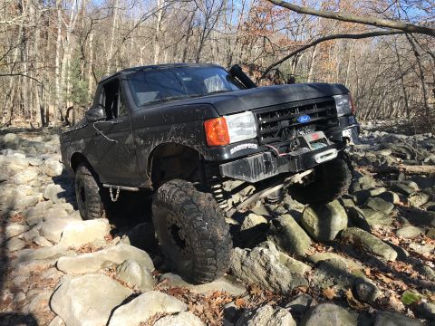 1989 Ford Bronco - A black Ford Bronco is shown off-roading through a challenging rocky landscape.